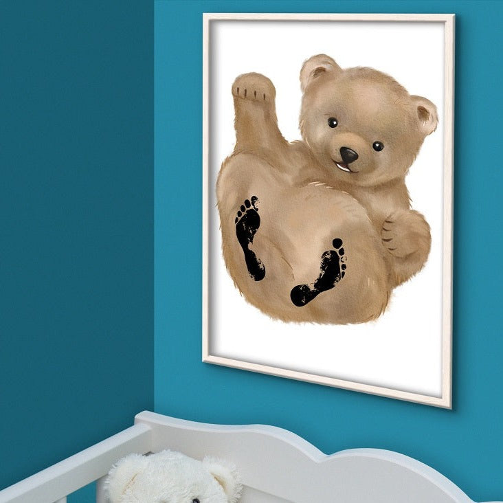 Babygeschenk mit Bären-Motiv hängt gerahmt an der Wand über dem Babybett mit einem Teddy darin. 